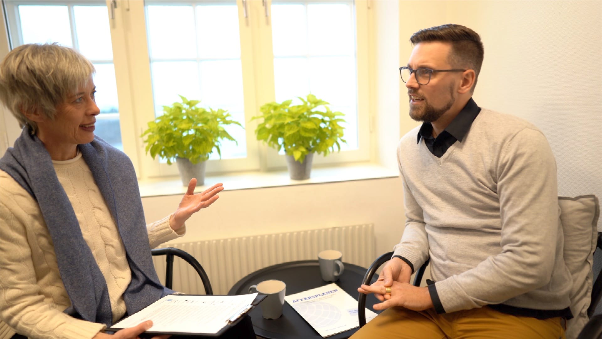 Två personer i samtal med broschyren Affärsplanen på bordet